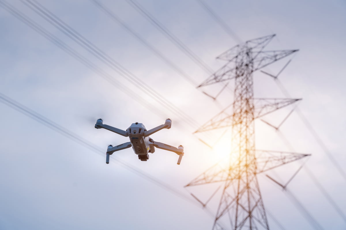 A four-rotor drone flying in front of a power line tower